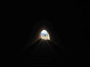 Image of a dark railway tunnel with the exit centered in the mid distance