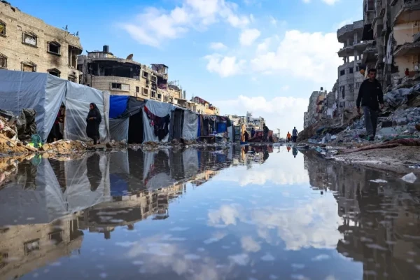 Displaced Palestinians walk around a puddle in front of destroyed buildings and tents in Khan Younis in the southern Gaza Strip [AFP]