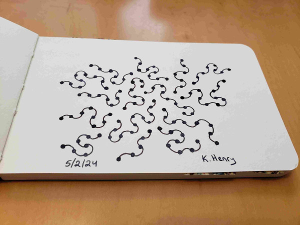 Hand drawn generative art in ink on an open page of my sketchbook. The abstract pattern looks a bit like squiggly worms with beads evenly spaced along their lengths.