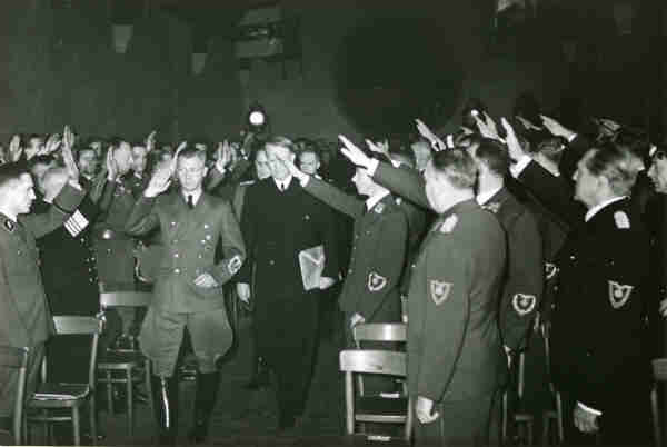 A B&W photo of Terboven in nazi uniform leading Quisling in a dark suit through a sea of uniformed men giving the nazi salute.