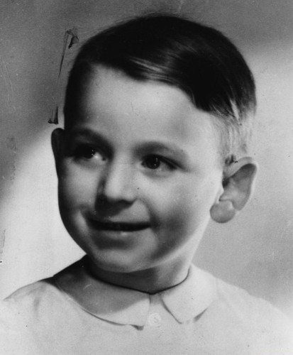 Black and white portrait of a young boy with short hair, smiling gently and looking slightly to the left. The child is wearing a light-colored shirt with a neat collar. The background is plain, enhancing the focus on the child's expression.