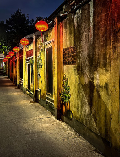 Narrow street in Hoi An, Vietnam. Painting of doors and potted plants adorn the golden walls illuminated the tradional handmade red silk lanterns.