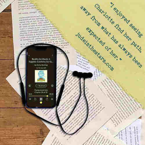 On a backdrop of book pages, an iPhone with the cover of Reality in Check (A South Downs Romance #2) by Emily Banting, narrated by Angela Dawe. In the top right corner of the image, a strip of torn paper with a quote: "I enjoyed seeing Charlotte find her path, away from what has always been expected of her." and a URL: judeinthestars.com.