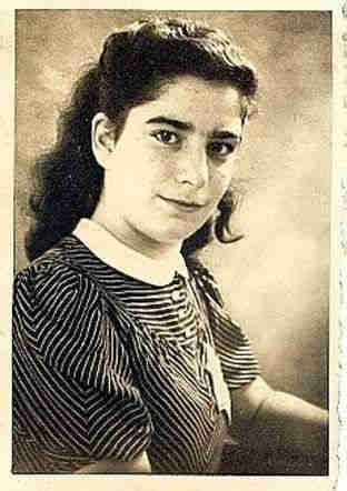 Portrait photograph of a teenage girl. She is wearing a short-sleeved blouse with black and white thin stripes. She has long, dark wavy hair pinned back. Her head is turned slightly towards the lens. She is looking straight into the lens.