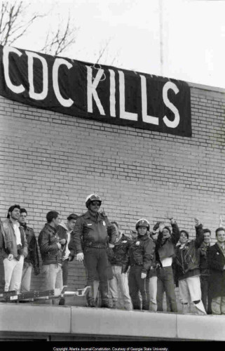 ACT UP protestors hang a banner, CDC KILLS, from the roof of a building at the U.S. Centers for Disease Control and Prevention, 1990.