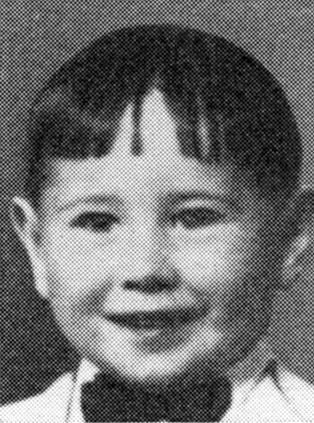 Black and white photo of a young child with a bow tie and a straight, short haircut, smiling at the camera.