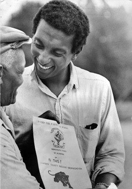 Stokely Carmichael, right, organizing local people for the Lowndes County Freedom Organization (LCFO) in 1966. His flyer features the original LCFO black panther logo. By Unknown author - Encyclopedia of Alabama, CC0, https://commons.wikimedia.org/w/index.php?curid=66872713