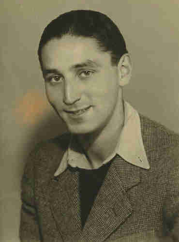 An ID portrait picture of a young man with short dark hair. He has a jacket, sweater and wide collar wite shirt. He is smiling. 