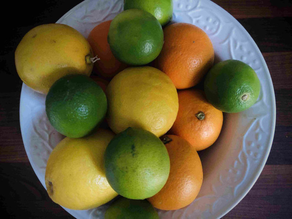 Eine Schüssel voller Zitronen, Orangen und Limonen, die alle dicht aufeinander liegen.