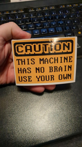 A warning  style sticker with yellow background and black old-school game typography reading: "Caution - This machine has no brain, use your own" in all caps