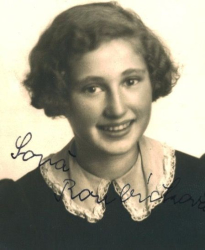 Vintage black-and-white portrait of a smiling young woman with curly hair, wearing a dark blouse with a light-colored, lace-trimmed collar. 