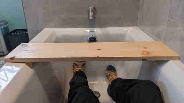 A man rests ina tub, with a wood board held resting neatly within the contours. 