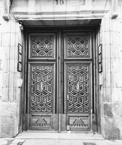 My photo with a black and white filter of an ornately carved set of double doors. 