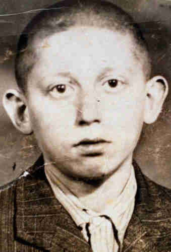 Black and white portrait photograph of a boy with very short hair and protruding ears. He is wearing a jacket and striped shirt. He has a sad expression on his face. 