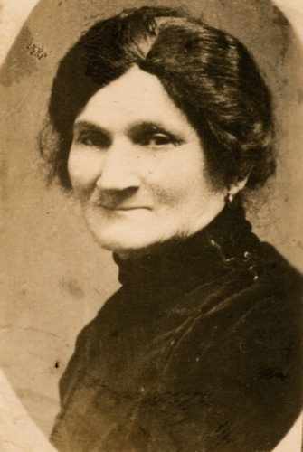Vintage portrait of a mature woman, wearing a dark high-collared dress, with her hair styled in a middle part and pulled back.