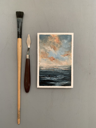 Original seascape oil painting by Tisha Mark, "Let's Dream" oil on Arches oil paper, 6"x4" (2024), shown with paint brush and palette knife for scale. Seascape painting with grayish-blue and orange cloud formations over a dark blue ocean with a rocky shore.