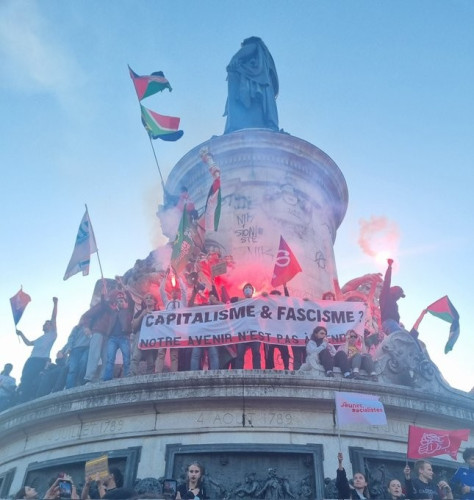 Protesters on the monument in Place de la République with an array of flags - including France Insoumise, South Africa and Palestine, lighting flares and holding a massive banner reading
CAPITALISM AND FASCISM?
OUR FUTURE IS NOT FOR SALE