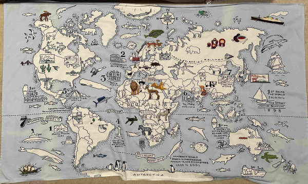A fabric map of the world. On the map there are lots of animals and landmarks. Some of these have been coloured in using embroidery.