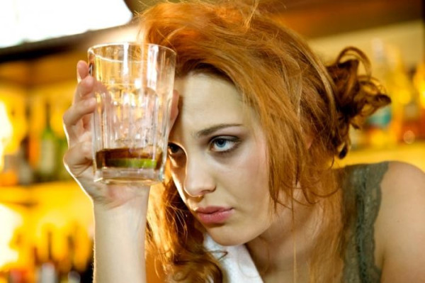 ginger-haired lady looking worse for wear holding a glass to her head.