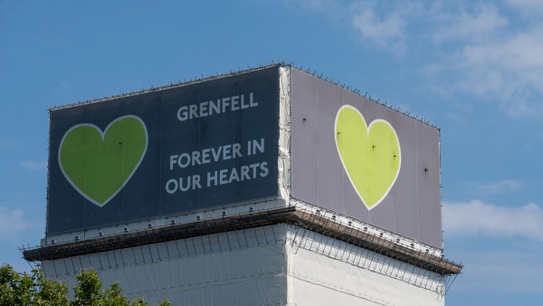 The top of the Grenfell Tower in Kensington & Chelsea, with a large grey poster bearing a green heart covering the top floor.  Text reads
GRENFELL
FOREVER IN OUR HEARTS