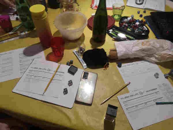 Tabletop roleplaying game table mid-game, showing Mail Order Apocalypse character sheets, dice, food and drinks.