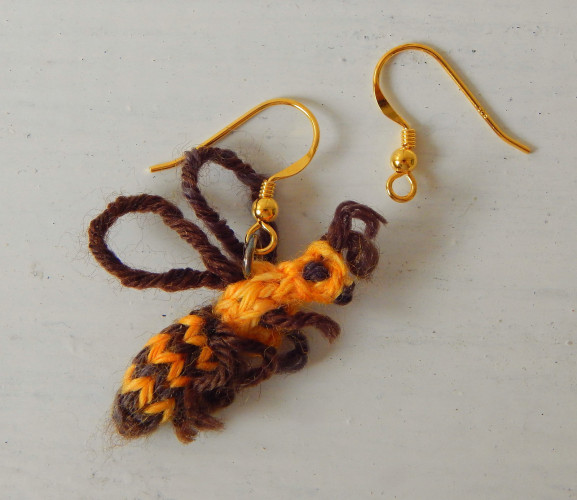 Close up of small knit bee in yellow and brown attached to earring.