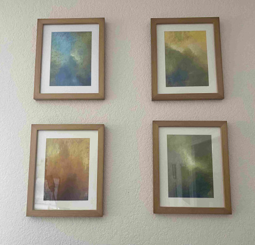 Four small framed paintings hang on a white wall. They are misty, out-of-focus abstract pieces.