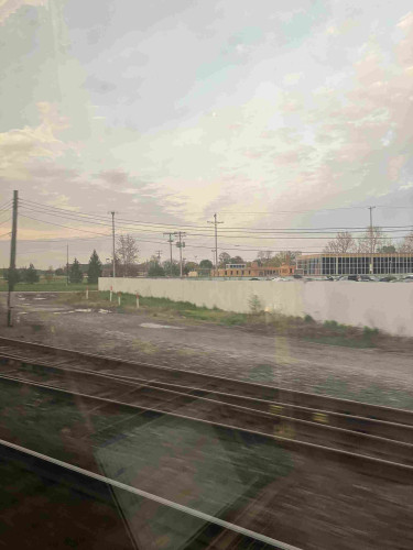 Photo out of train window. Foreground: rails. Background: misc office buildings and a large white wall. Telephone poles dot the landscape. Again, it looks like I’ve applied an instagram filter. Again, the windows are just dirty/tinted