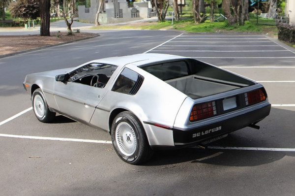 A picture of a delorean ute in a parking lot in a woody neighbourhood. Its rear tray is designed like a cybertruck.