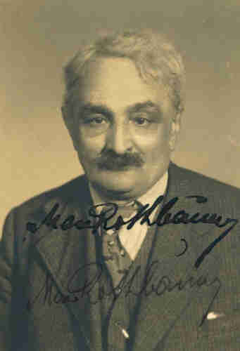 Photo for documents of an elderly man. He has grey hair and a luxuriant moustache. He is dressed in a jacket, waistcoat, shirt and tie. His handwritten signature can be seen on the photo.