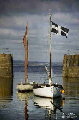 Two small boats, one flying the 'Cornish' flag of St Piran, in the entrance to the small harbour at Mousehole, near Penzance.
