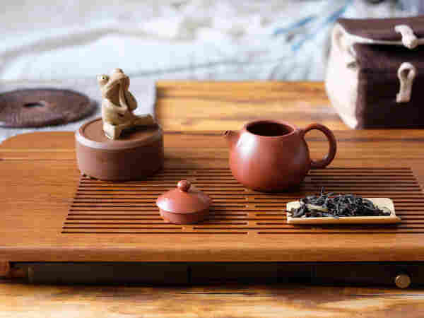 dry tea leaves next to clay teapot