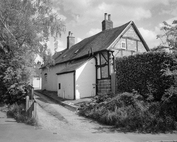 The back and end of a row of cottages. The end wall is "half-timbered" with the structure supported by old black beams, and the bricks at different angles filling in the gaps (where whattle and daub plast would have been. Black and white photo.