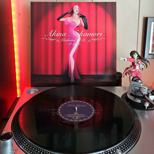 A vinyl record sits on a turntable. Behind the turntable, a vinyl album outer sleeve is displayed. The front cover shows Akina Nakamori dressed up as Jessica Rabbit standing on a stage in front of a curtain, with a spotlight on her. 