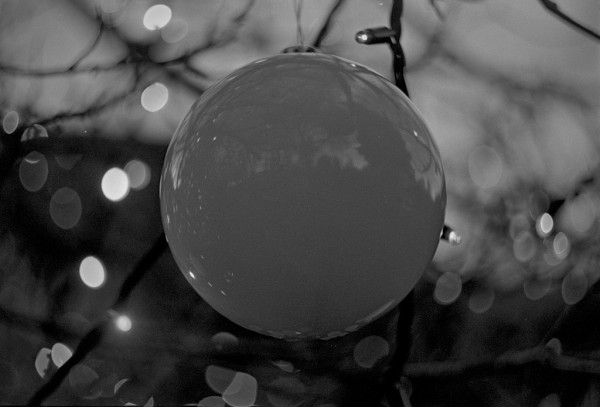 A large glass globe hanging in a tree dominates the centre of this black and white photo, with  Christmas lights surrounding it, distorted by the swirly bokeh of the Helios lens.