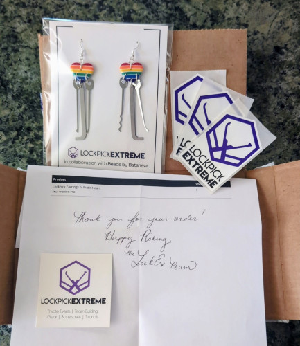 Unboxing of my new Pride heart lockpick earrings from Lockpick Extreme, including the earrings, stickers, a business card, and a written thank you note on the packing slip.