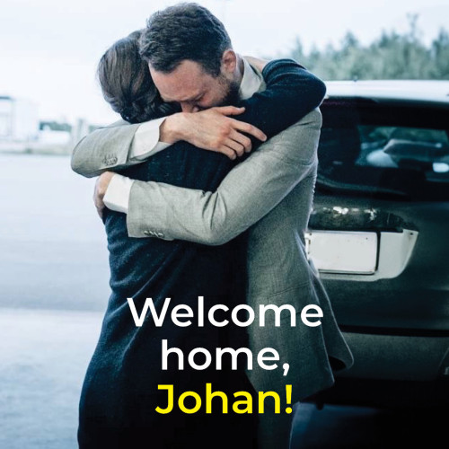 The image shows two people embracing each other warmly, standing next to a car. The background is slightly blurred, focusing the attention on the embrace. The text in bold at the bottom of the image reads:

"Welcome home, Johan!"