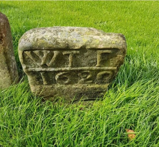 An rectangular ancient stone or waystone marker in a green field with long grass. It's engraved with "WTF" and "1620" taking up most of the surface area