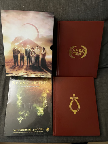 Masks of Nyarlathotep Deluxe Edition

Slipcase with expedition in front of a pyramid with a sunset in the background.

Keeper’s Screen and Handouts.

Two red faux leather volumes with arcane symbols in gold. 