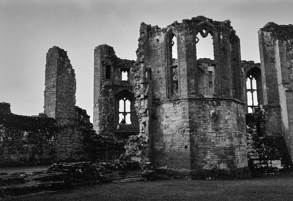 The ruins of stone buildings within the Castle can be seen. High walls with tall windows in them. In one window, a figure is silhouetted. Black and white photo.