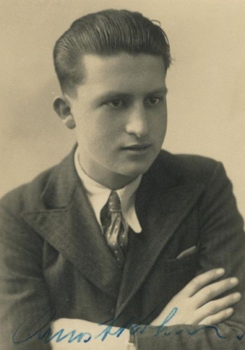 Vintage black-and-white portrait of a young man wearing a suit and tie, featuring a hairstyle typical of the early to mid-20th century, and including a signature at the bottom of the image.