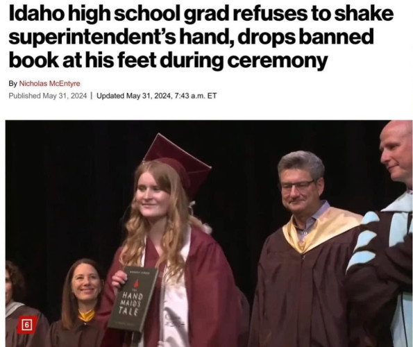 Screenshot of news report with a photo of a female in graduation attire holding a copy of The Handmaid’s Tale:

Idaho high school grad refuses to shake superintendent's hand, drops banned book at his feet during ceremony
