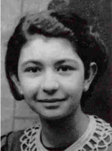 A photograph of a young girl's face. She is slightly smiling about looking into the lens. She is wearing a patterned collar. She has dark hair. 