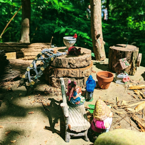 fairy garden with gnomes, tiny garden pots and bench, and twig ladder with flowers