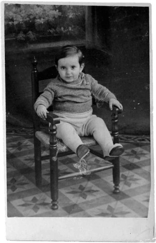 A vintage black and white photo of a little child seated on a wooden chair.