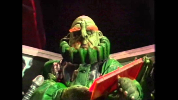 Picture a Vogon Captain -  a green humanoid creature , some what bigger than a human, with very bushy red eyebrows & a very stern demeanour! - sitting  in a suitably large chair , wearing a green one piece jumpsuit with a high collar & reading poetry from a large red bound book.