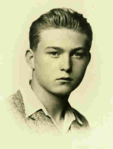 An ID portrait photo of a teenager. He has short hair combed to the back. You can see he is wearing a jacked and unbuttoned shirt.