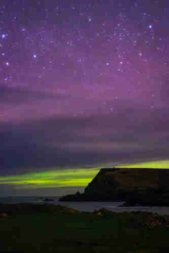 A night sky of stars, purples and greens of the Aurora Borealis, with Glen Head cliff face in profile jutting into the Atlantic in the bottom third of the image. 
Glencolmcile, Co Donegal, Spring 2024.