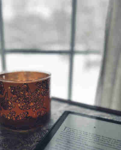 The glow of a candle, next to my Kindle, and the window in the background looks out to a snowy backyard. 