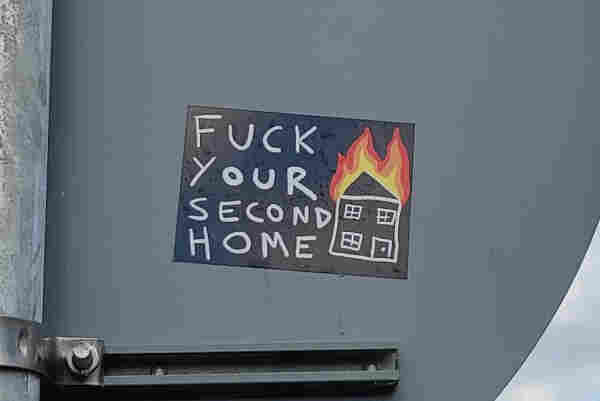 Sticker on a sign featuring a burning house and the words"Fuck your second home"